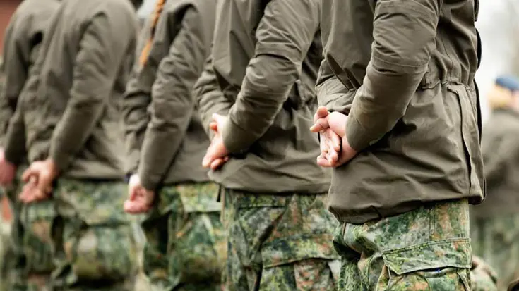 Vijf militairen zij aan zij schuin van achteren gefotografeerd.