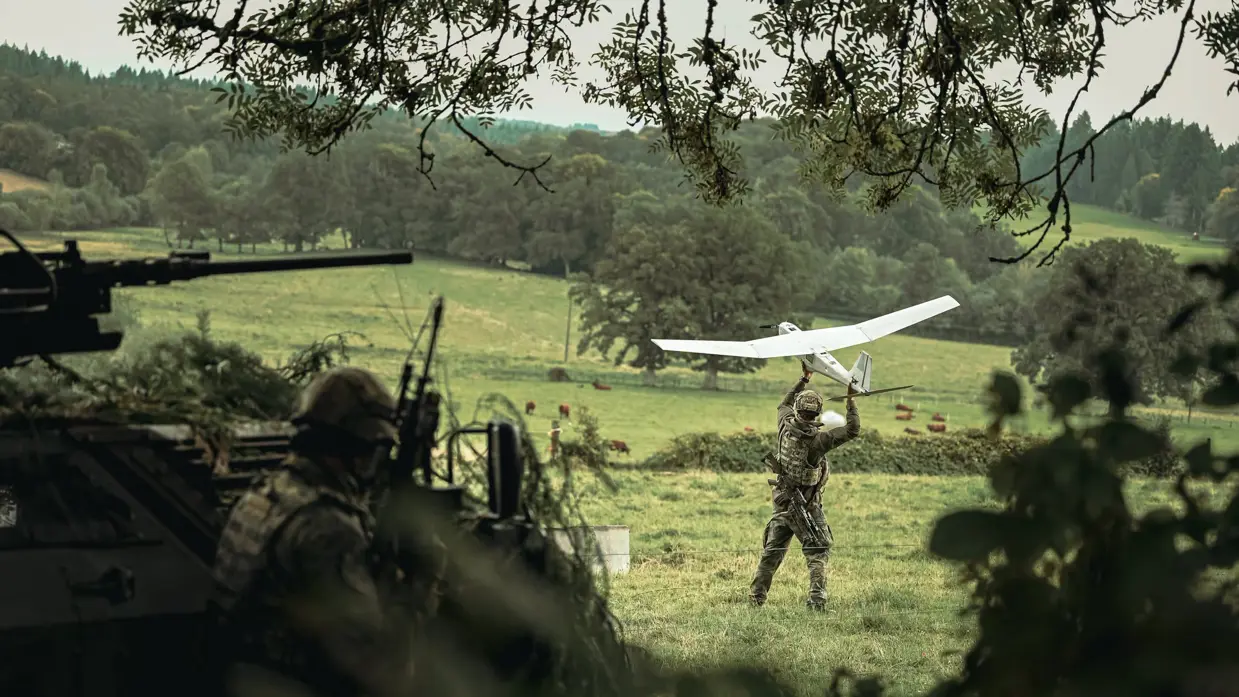 Militairen en een drone in en net naast een bosrand.
