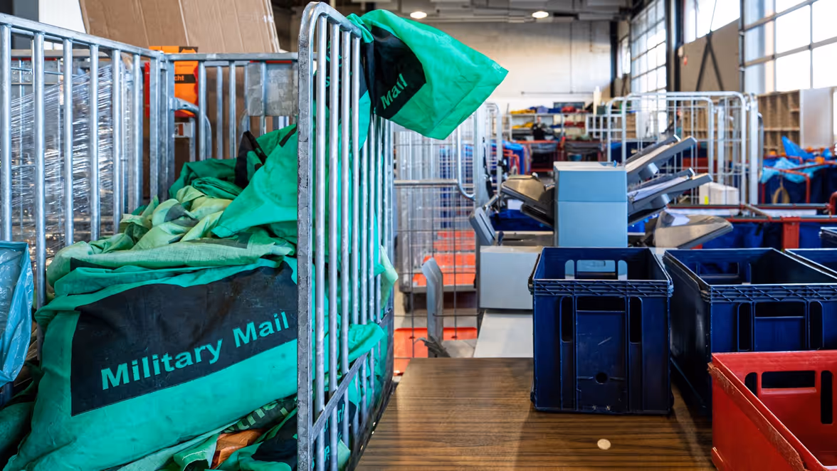 Een militaire postkamer met een rolcontainer en plastic bakken.