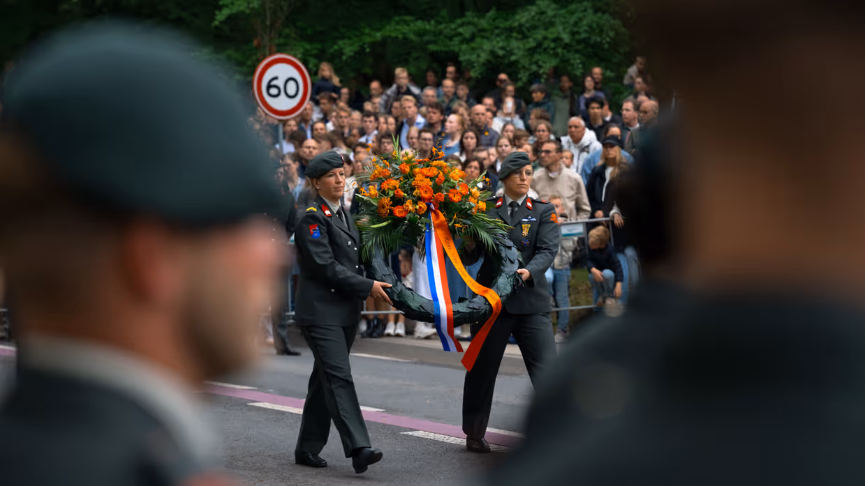 Luitenant Kleinbloesem spreekt reservisten toe Twee reservisten lopen met een krans 