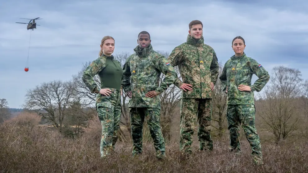 Militairen kijken in de camera, staan in het veld en dragen een vlekkenpak