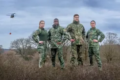 Militairen kijken in de camera, staan in het veld en dragen een vlekkenpak