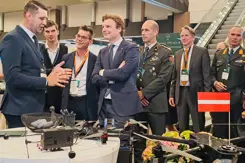 Brekelmans en anderen luisteren bij tafel met drone naar uitleg.