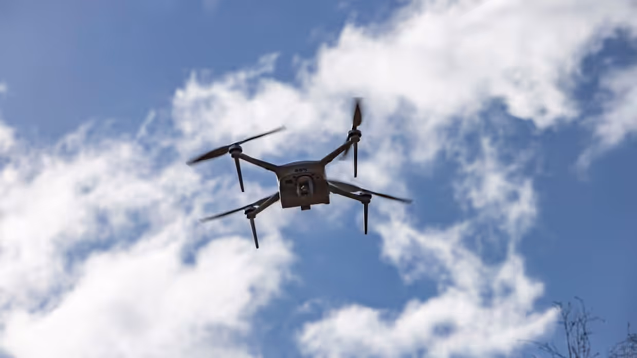 Een drone vliegt door de strak blauwe lucht.  