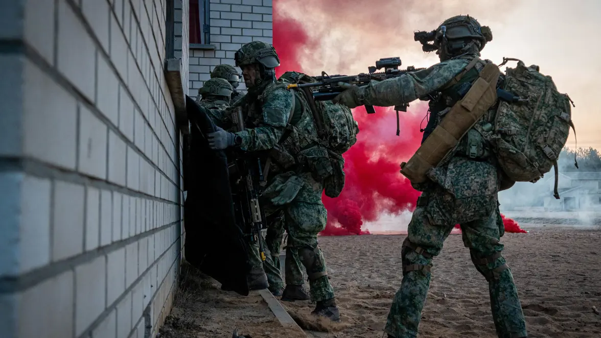 Militairen naast rode rook naast een gebouwtje.