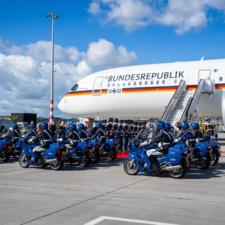 Motorrijders en Marechaussees in ceremonieel tenue voor het Duitse regeringsvliegtuig.