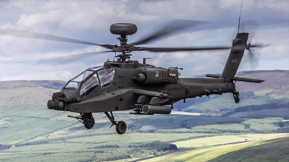 Een lviegende Apache gevechtshelikopter met heuvels op de achtergrond.