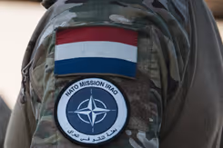 Schouder militair met NAVO-embleem en Nederlandse vlag erboven.