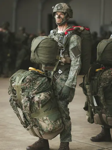 Een parachutist van 11 Luchtmobiele Brigade staat met volledige spronguitrusting en zware bepakking gereed voorafgaand aan een airborne-operatie tijdens oefening Versatile Guard.