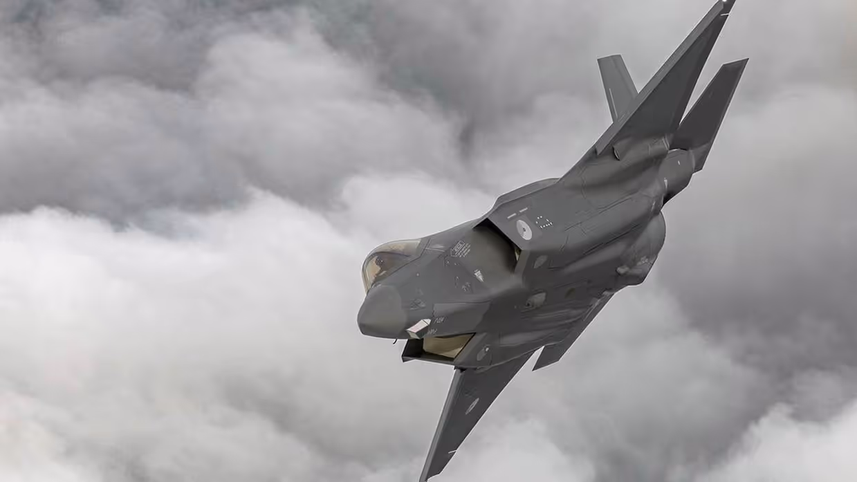 F-35 schuin in een bocht met op achtergrond dik grijs wolkendek.