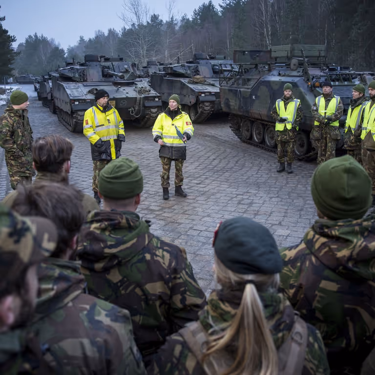 Militairen luisteren in kring naar collega's met gele hesjes.