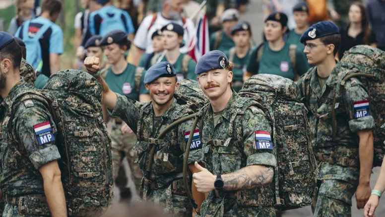 Twee militairen van de Marechaussee tijdens de 4Daagse, in groen tenue, steken hun duim op naar de camera.