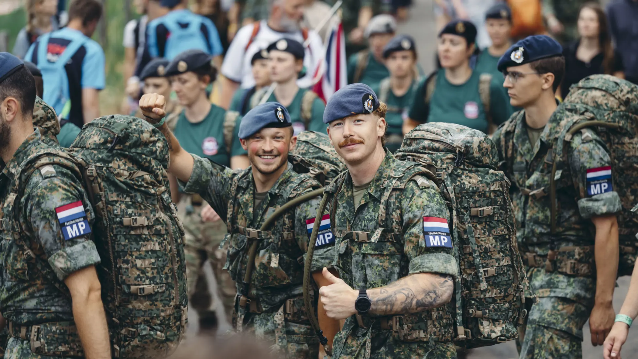 Twee militairen van de Marechaussee tijdens de 4Daagse, in groen tenue, steken hun duim op naar de camera.