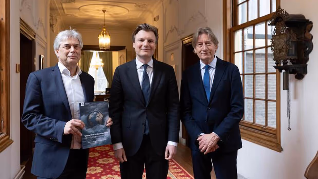 Drie mannen in pak staan naast elkaar. De man links houdt een rapport vast.