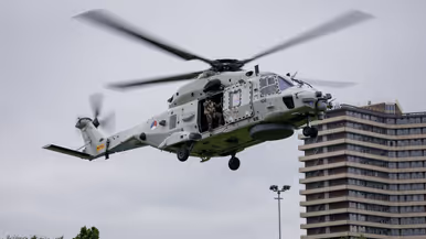 Een Chinook stijgt op boven een veld, met aan een lange kabel de Nederlandse vlag