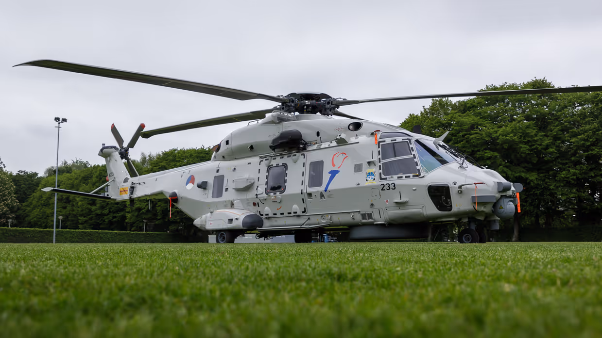 Een Chinook stijgt op boven een veld, met aan een lange kabel de Nederlandse vlag