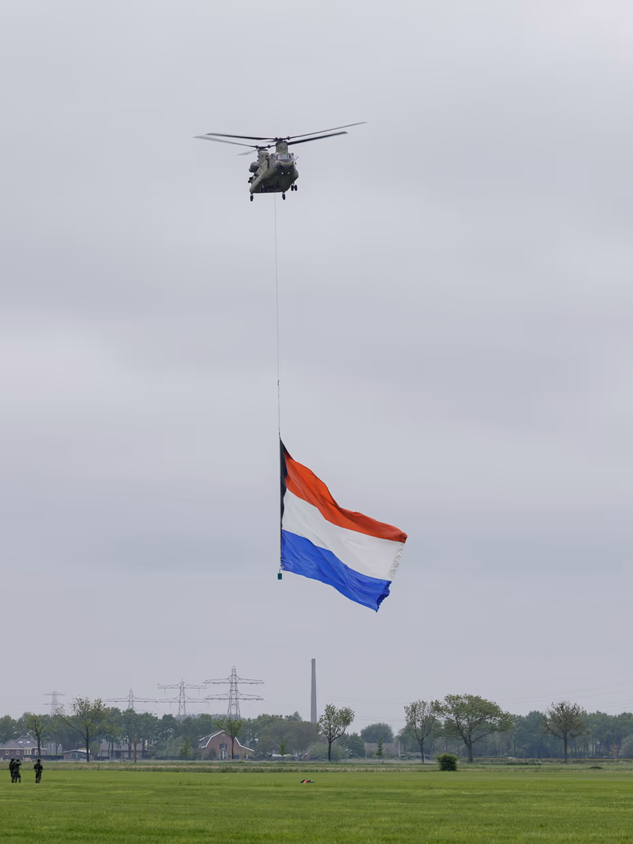 Een Chinook stijgt op boven een veld, met aan een lange kabel de Nederlandse vlag