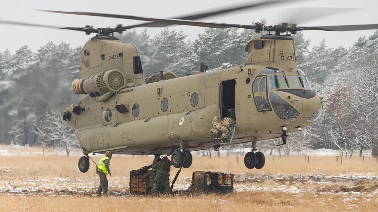 Een helikopter maakt een landing op een wit veld. Rechts met een paar pakketten onder zich. 