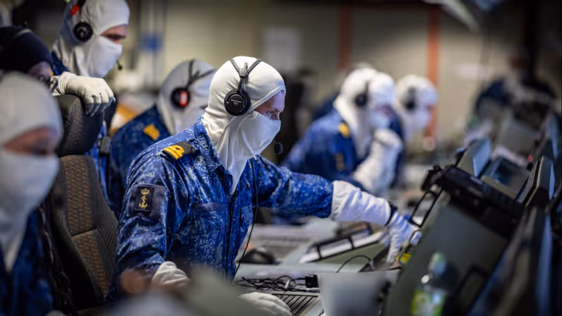 Marinepersoneel zit in een ruimte vol computers. Ze dragen witte bivakmutsen.