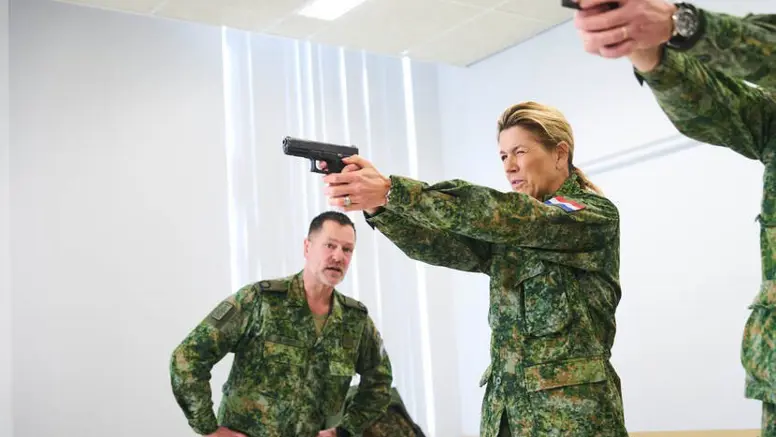 Alt-tekst: Koningin Maxima richt een wapen. 
