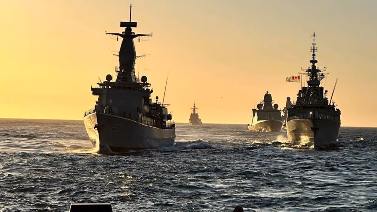 Varende militaire schepen met pastelkleurige lucht als achtergrond.