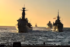 Marineschepen varen achter elkaar op zee.