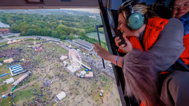  Zangeres Maan zwaait door de open deur van een vliegende heli naar publiek op het festivalterrein onder hen.