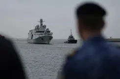 Het grijze schip De Vlissingen komt aangevaren. Rechts vaag een marinier in beeld.