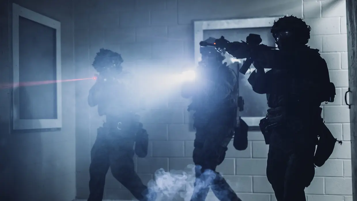 Drie mariniers die hun laserdots gebruiken bij de instap van een slecht verlichte kamer. 
