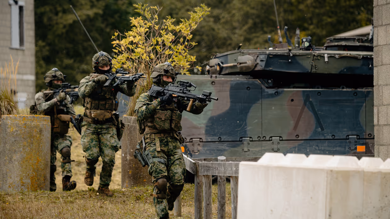 Drie militairen lopen langs een voertuig met getrokken geweren.