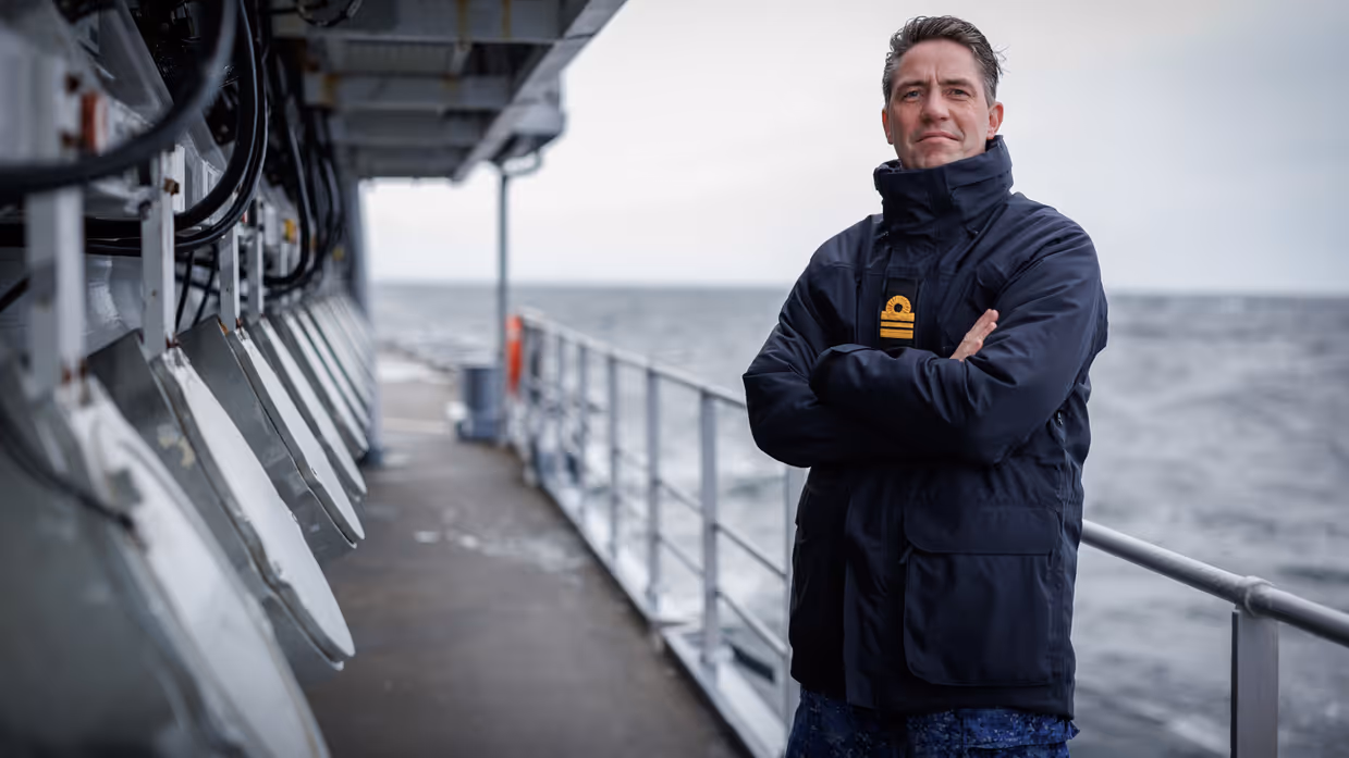 Een militair poseert langs de railing van een schip.