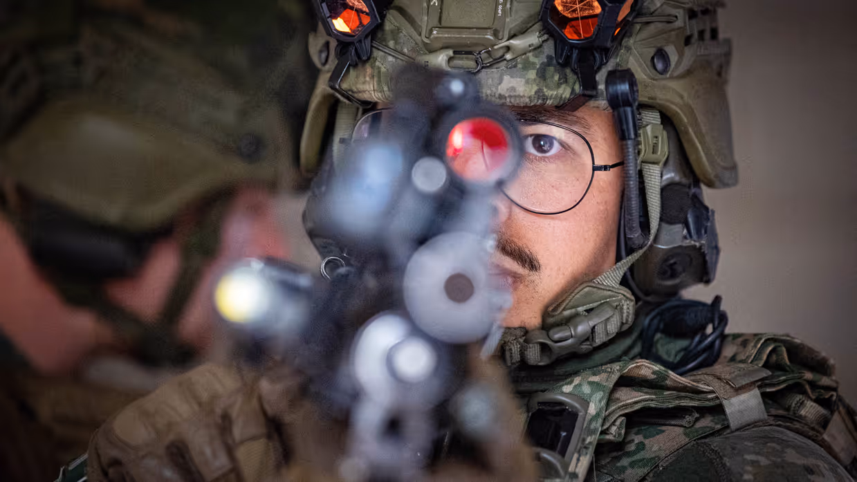 Een close-up van een militair met zijn geweer in de voorgrond.