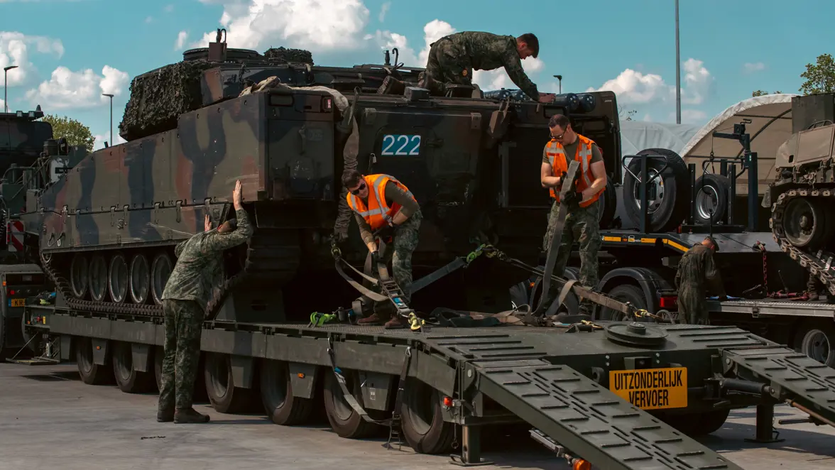 Militairen zetten een pantservoertuig vast op een vrachtwagen. 