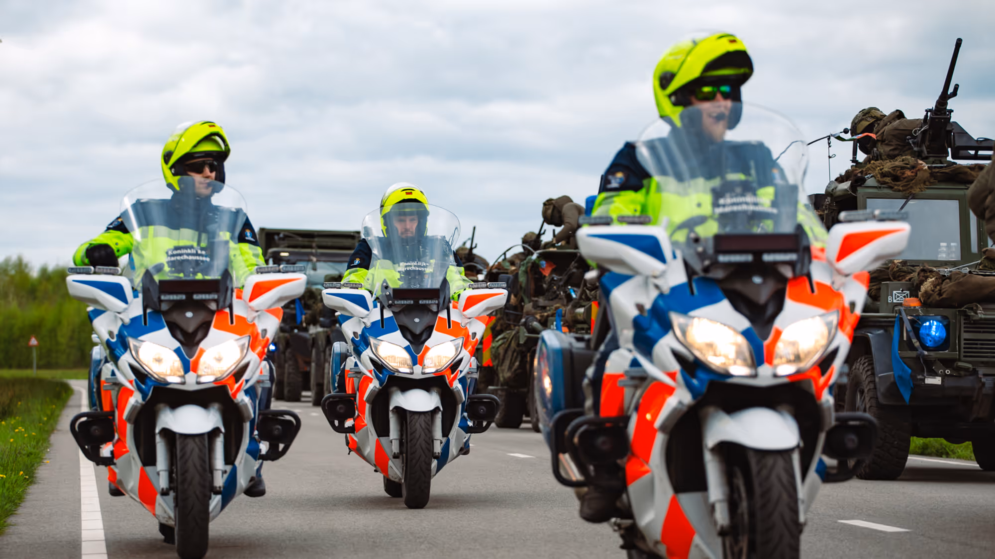 Motoren marechaussee rijden naast militaire voertuigen.