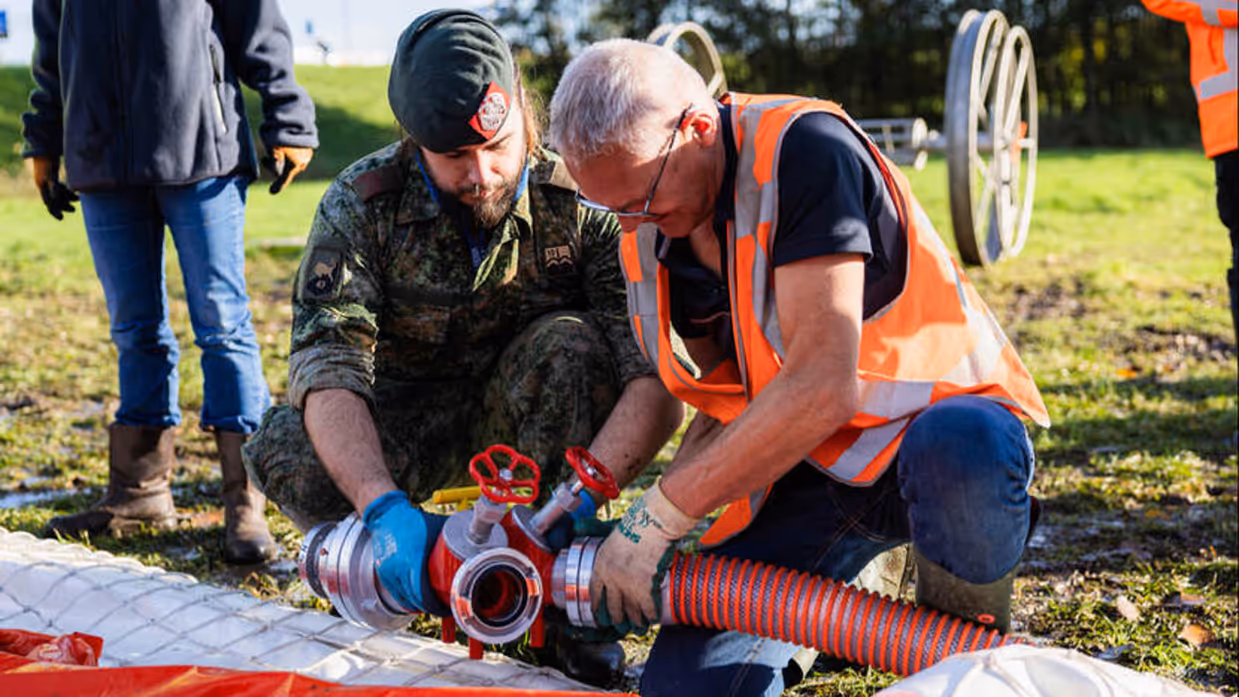 En waterschaps- en een defensiemedewerker zitten gebukt bij een rode slang.