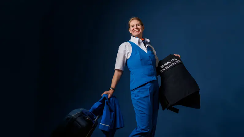Portret van adjudant Elviera in KLM-pakje en met KMar-jas in de hand.