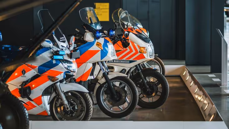 Rood-blauw gestreepte motoren van de marechaussee op de museumvloer.