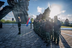 Militairen staan in de houding terwijl een van hen de Nederlandse vlag vasthoudt.
