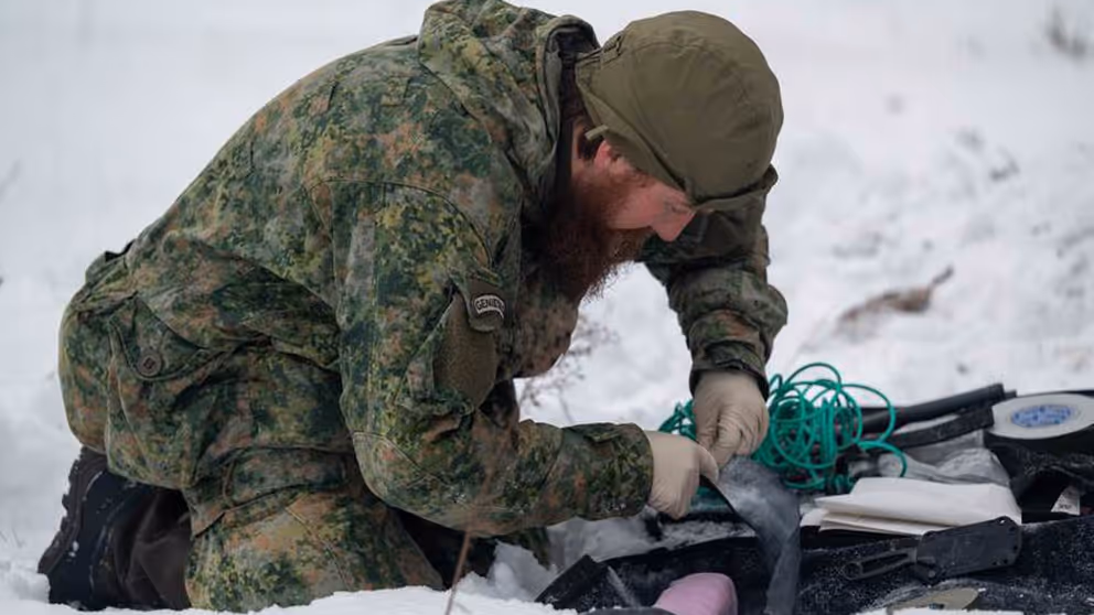 Militair op knieen in de sneeuw bezig met bevestiging van draden.