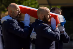 Militairen dragen kist met Nederlandse vlag tijdens herbegrafenis.