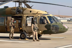 Dozen met hulpgoederen staan in een helikopter met de deur open. 2 militairen staan naast de helikopter..