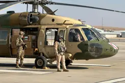 Dozen met hulpgoederen staan in een helikopter met de deur open. 2 militairen staan naast de helikopter..