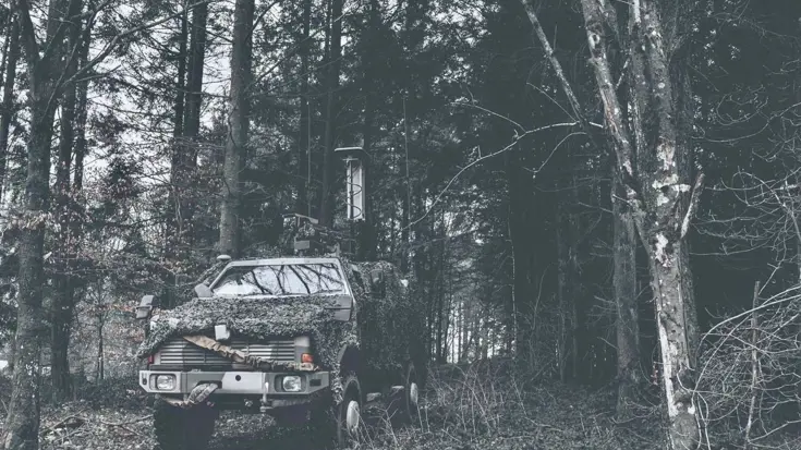Jeep met camouflage net in het bos.