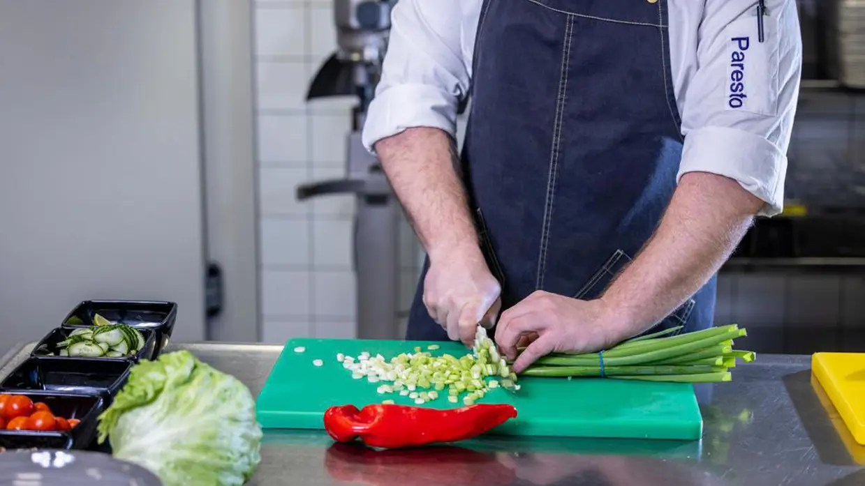 Op de linkerfoto een mooi opgemaakt bord met een gerecht dat bestaat uit onder andere aardappel en wortel. Op de rechterfoto snijdt een Paresto-keukenmedewerker een aantal lente-uitjes.