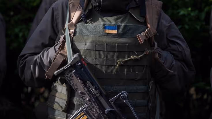 Vest van militair met Oekraïense vlag erop. Voor de borst hangt een machinegeweer.