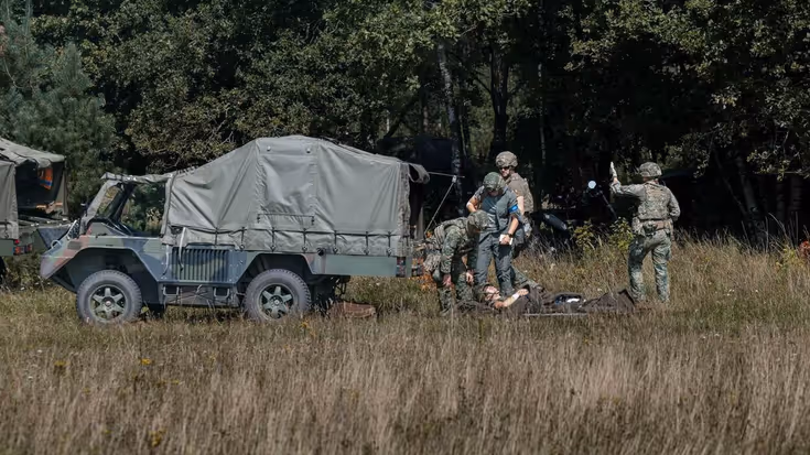 4 militairen met een gewonde op brancard staan achter een Boxer-ambulance.