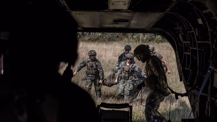 Militairen lopen met brancard naar ambulance. Foto gemaakt vanuit de ambu.