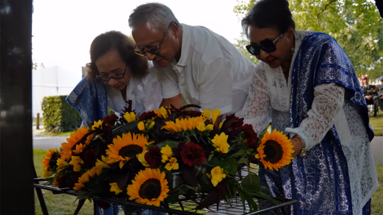 3 mensen leggen een krans met zonnebloemen bij het monument.