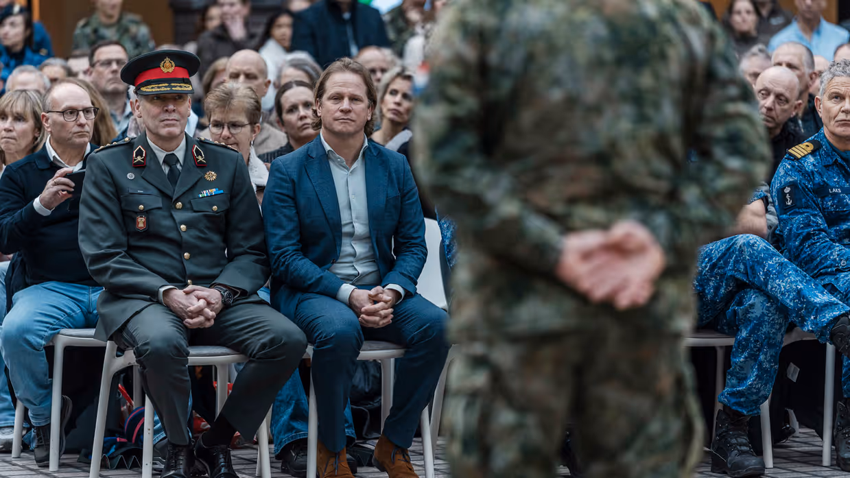  links: de staatssecretaris zit op een stoel. Rechts: Militairen lopen langs andere militairen
