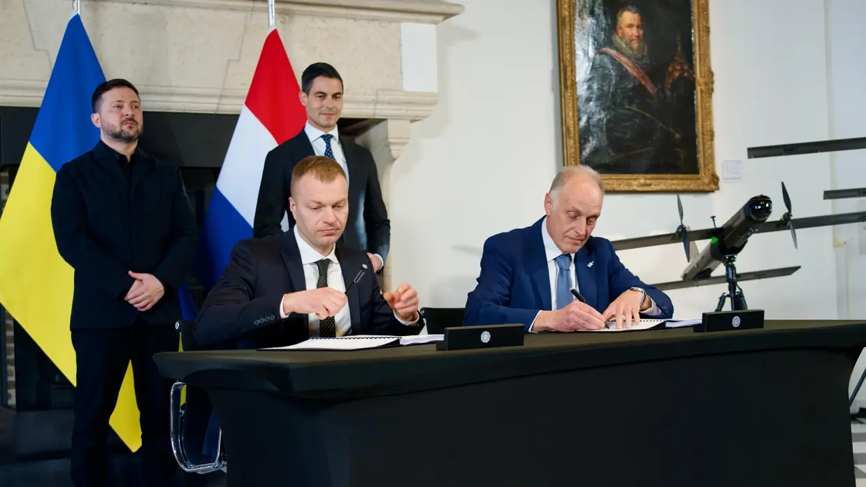 Twee mensen ondertekenen een document dat op de tafel voor hen ligt. 